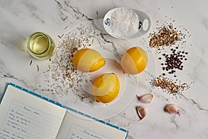 Top view of a marble table with a notebook with a recipe, lemon, garlic, and spices