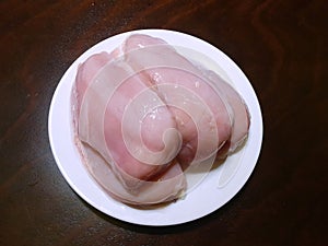 Top view of marinated chicken fillet on white bowl on wooden table as a background