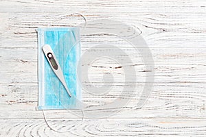 Top view of medical protective mask and digital thermometer on white wooden background. Health care concept with copy space