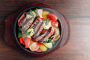 Top view of medium rare beef steak served in hot plate with tomato, bell pepper, radish and rosemary