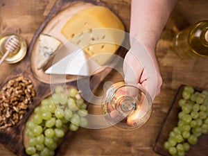 Top view of men`s hand holding a glass of wine next to various cheeses