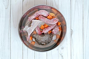 Top view on metal pet bowl with chicken necks, beef paunch pieces and cut carrot.