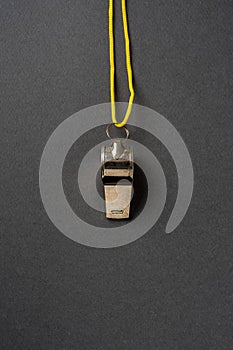 Top view of metal whistle with yellow string on dark gray background