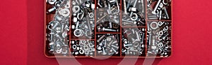 Top view of metal wood screws and nuts in tool box on red background, panoramic shot