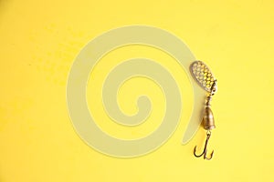 Top view of a metallic fishing lure isolated on a yellow background