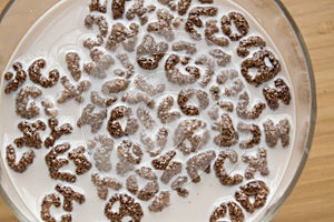 Top view of milk bowl, alphabet letters of cereal and chocolate flakes on wooden table, healthy Breakfast for kids and adults,