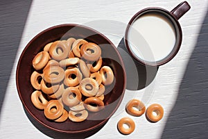 Milk in a brown ceramic cup and small dry bagels for kids on white wooden background. First solid finger food for baby. Healthy me