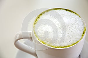 Top view of milk green tea matcha latte with the saucer on white table background. Hot milk green tea (selective focus)