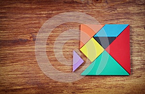 Top view of a missing piece in a square tangram puzzle, over wooden table.