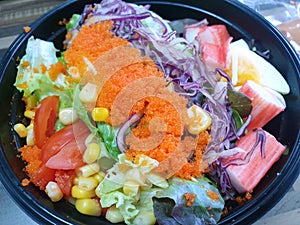 Top view of mixed vegetable salad with fresh lettuce, green oak, bread, boiled egg, flying fish and salad dressing in black bowl a