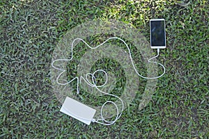 Top view of mobile phone equipment placed on the grass power bank and charging cable