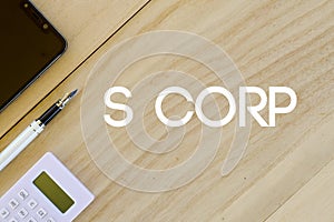 Top view of mobile phone,pen and calculator on wooden background written with S Corp. Business and finance concept. photo