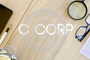 Top view of mobile phone,pen,clock,calculator,glasses,and magnifying glass on wooden background written with C Corp.