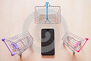 Top view on a mobile phone two food carts and a basket on a wooden table. Online shopping on a smartphone. Thumbnails.