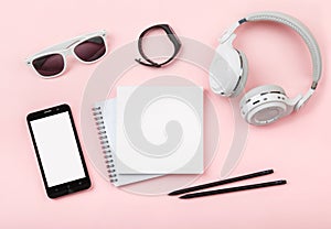 Top view mock up with phone, Fitness tracker, headphones, glasses, notebook on pink background.