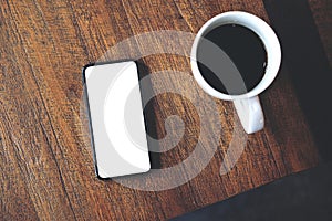 Top view mockup image of a black mobile phone with blank white desktop screen with coffee cup
