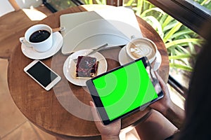 Top view mockup image of hands holding black tablet pc with blank green screen