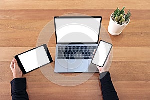 Top view mockup image of a hands holding mobile phone , black tablet and laptop with blank white screen