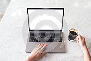 Top view mockup image of hands using laptop with blank white desktop screen and holding coffee cup on marble table