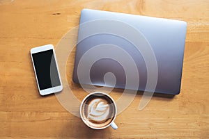 Top view mockup image of a white mobile phone with blank black desktop screen with laptop and coffee cup