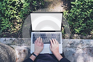 Top view mockup image of a woman using and typing on laptop with blank white screen , sitting at outdoor with nature