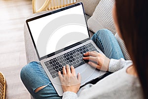 A woman working and typing on laptop computer with blank screen while sitting on a sofa at home