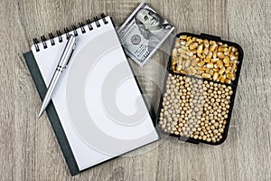 Top view mockup of open blank notebook on spiral, automatic pen. 100 dollar banknotes and samples of soybean and corn seeds