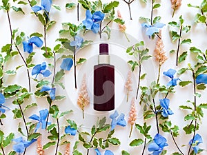 Top view of mockup of unbranded brown plastic spray bottle and floral decor - fresh greens, blue and pink flowers on a white