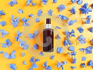 Top view of mockup of unbranded brown plastic spray bottle and petals of blue hydrangea flowers on a textured bright orange yellow