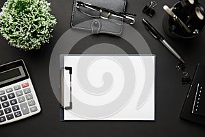 Top view of modern black office desk with blank paper sheet, notebook, pen and a lot of things. Flat lay table layout. Copy space