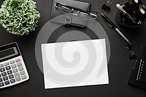 Top view of modern black office desk with blank paper sheet, notebook, pen and a lot of things. Flat lay table layout. Copy space