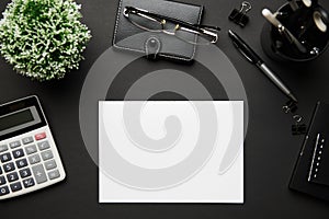 Top view of modern black office desk with blank paper sheet, notebook, pen and a lot of things. Flat lay table layout. Copy space