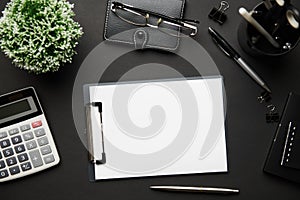 Top view of modern black office desk with blank paper sheet, notebook, pen and a lot of things. Flat lay table layout. Copy space