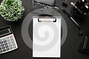 Top view of modern black office desk with blank paper sheet, notebook, pen and a lot of things. Flat lay table layout. Copy space