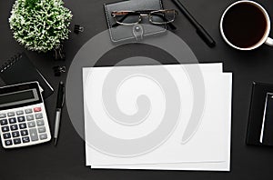 Top view of modern black office desk with blank paper sheet, notebook, pen and a lot of things. Flat lay table layout. Copy space