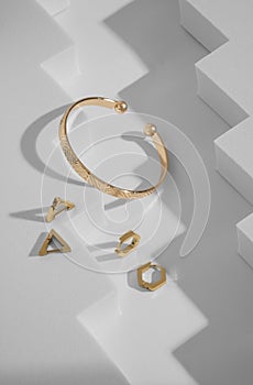 Top view of modern design golden bracelet and earrings on geometric white background