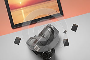 Top view modern digital camera and tablet with a photograph of the sea landscape on a gray-orange background