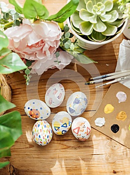 Top view of modern easter eggs painted. Brushes and paints with flowers and plants. Happy easter concept on a wooden background