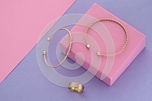 Top view of modern golden bracelets and ring on pink podium on purple background with copy space