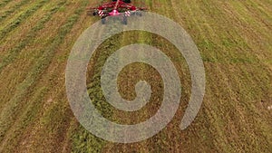 Top view of modern tractor with working red round rakes runs on mowed field