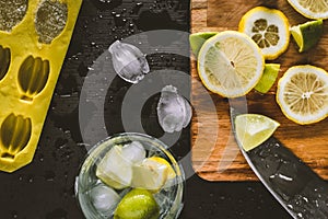 Top view of mojito preparation with sliced lemons, ice cubes, and knife on the counter