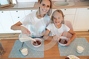 Top view of a mom pouring milk to her daughter for breakfast with chocolate flakes. have a good time together, dressed alike