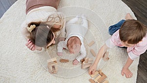 Top view of mother with baby and older son playing on carpet with toy wooden blocks. Parenting, children happiness and