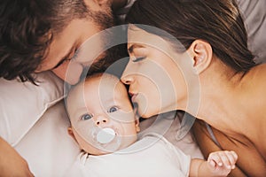 Top view. Mother and Father Kisses Baby in Bed.