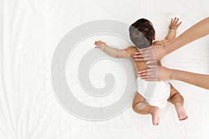 Top view of mother and her cute child on white bed. Baby massage and exercises