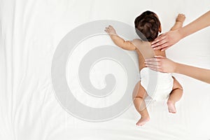 Top view of mother and her cute child on white bed. Baby massage and exercises