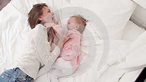 Top view Mother and little daughter tickle having fun jumping and playing funny active game in parents bed, Bouncing