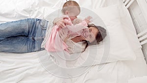 Top view Mother and little daughter tickle having fun jumping and playing funny active game in parents bed, Bouncing