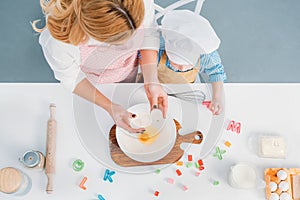 Top view of mother and son pouring egg into bowl