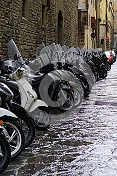 Florence, Italy - August 30 2023: Motorcycles and motor scooters parked in a row on a sidewalk.